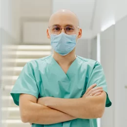 Confident healthcare worker in scrubs and mask with arms crossed.