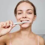 Woman smiling while brushing her teeth with a white toothbrush.