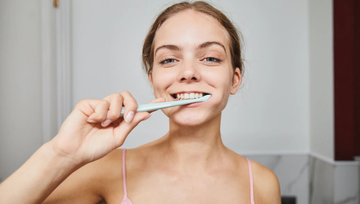 Woman smiling while brushing her teeth with a white toothbrush.