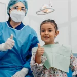 Dentist and young girl both giving thumbs up in a dental clinic.