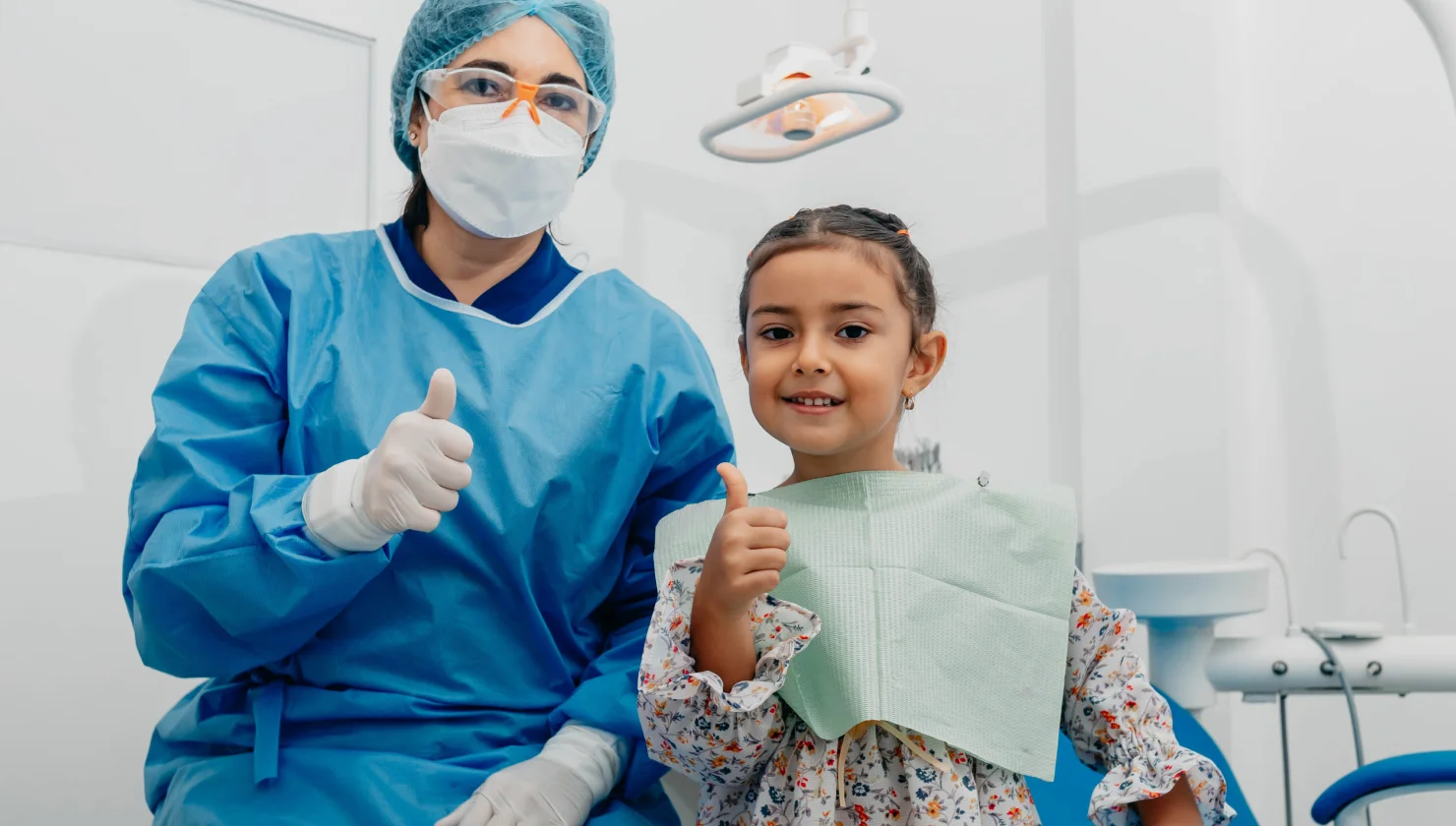 Dentist and young girl both giving thumbs up in a dental clinic.