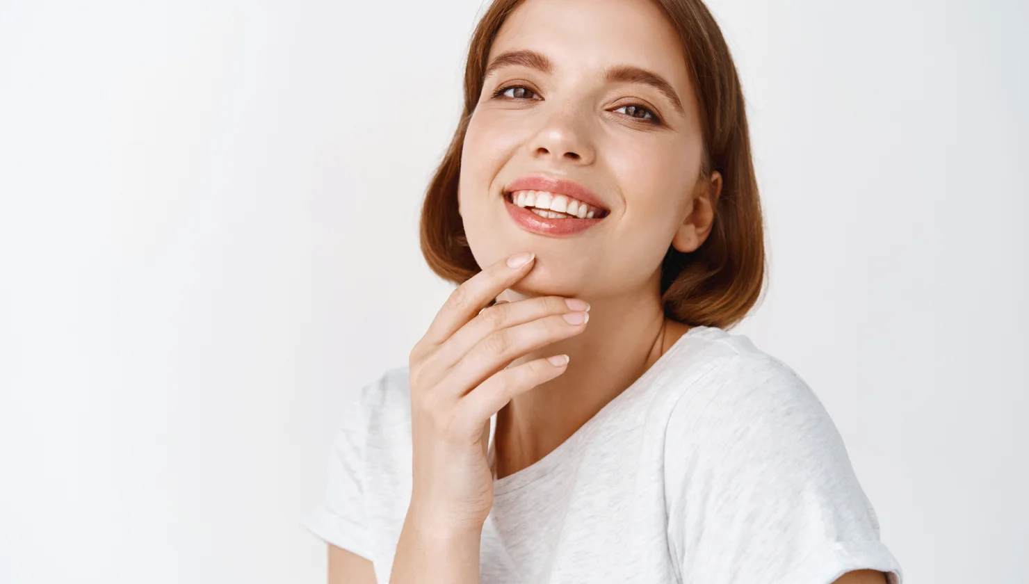 Smiling young woman with hand near chin, wearing white top.
