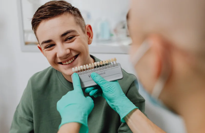 Dentist matching dental veneers for a smiling young man.