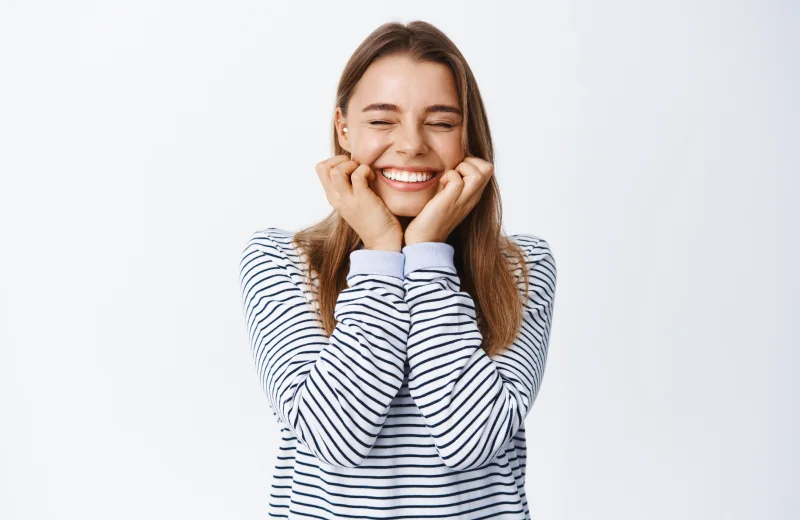 A joyful woman smiling with eyes closed, wearing a striped shirt.