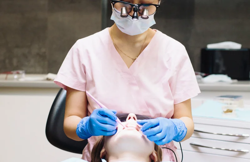 A dentist wearing a mask and gloves examining a patient's teeth.