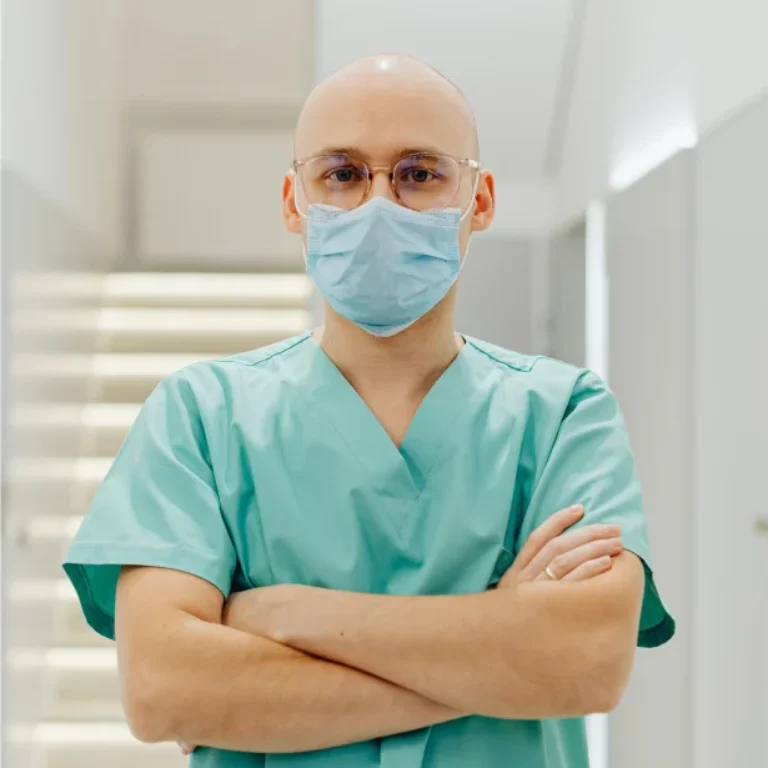 Confident healthcare worker in scrubs and mask with arms crossed.