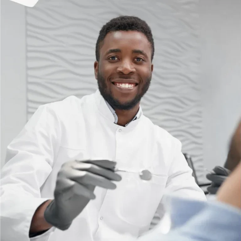 A smiling dentist wearing gloves treats a patient.