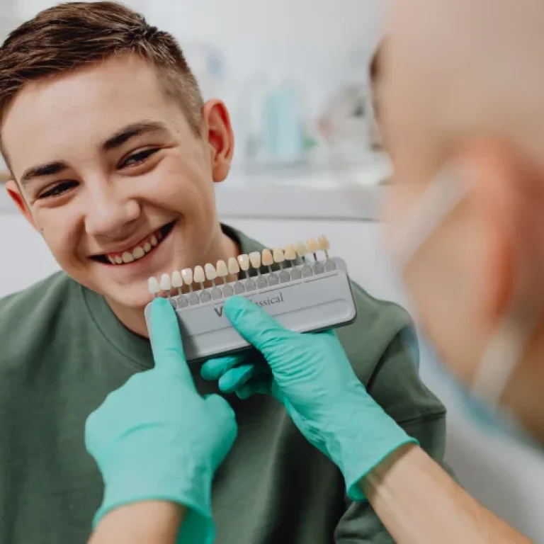 Dentist matching dental veneers for a smiling young man.