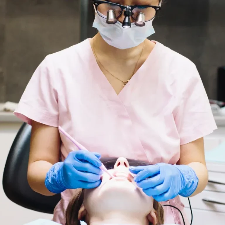 A dentist wearing a mask and gloves examining a patient's teeth.